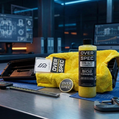 Over Spec car care products including a bottle and towel on a workbench with a blurred background.